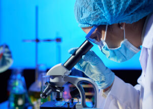Profile view of concentrated Asian microbiologist examining sample with help of modern microscope while wrapped up in work at dim laboratory