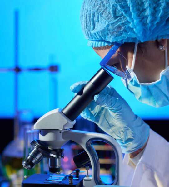 Profile view of concentrated Asian microbiologist examining sample with help of modern microscope while wrapped up in work at dim laboratory