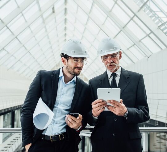 two-successful-entrepreneur-helmet-with-project-laptop-new-buildings-stay-near-glass-roof_496169-971