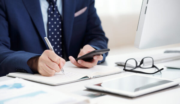 Cropped image of businessman checking messages in smartphone and taking notes in planner